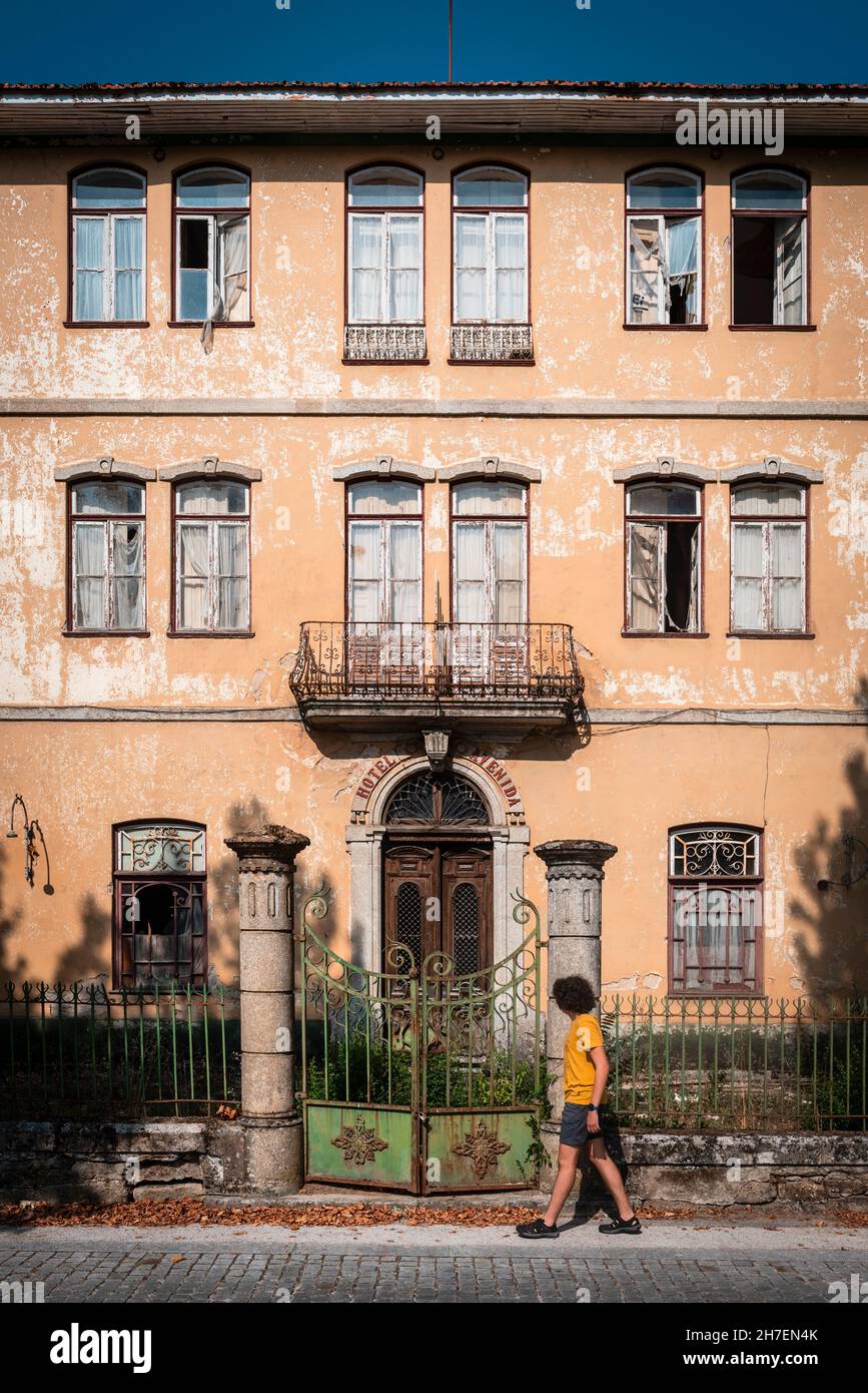 Fenêtres, porte d'entrée et clôture d'entrée d'un ancien manoir abandonné avec un garçon passant sur le trottoir. Banque D'Images