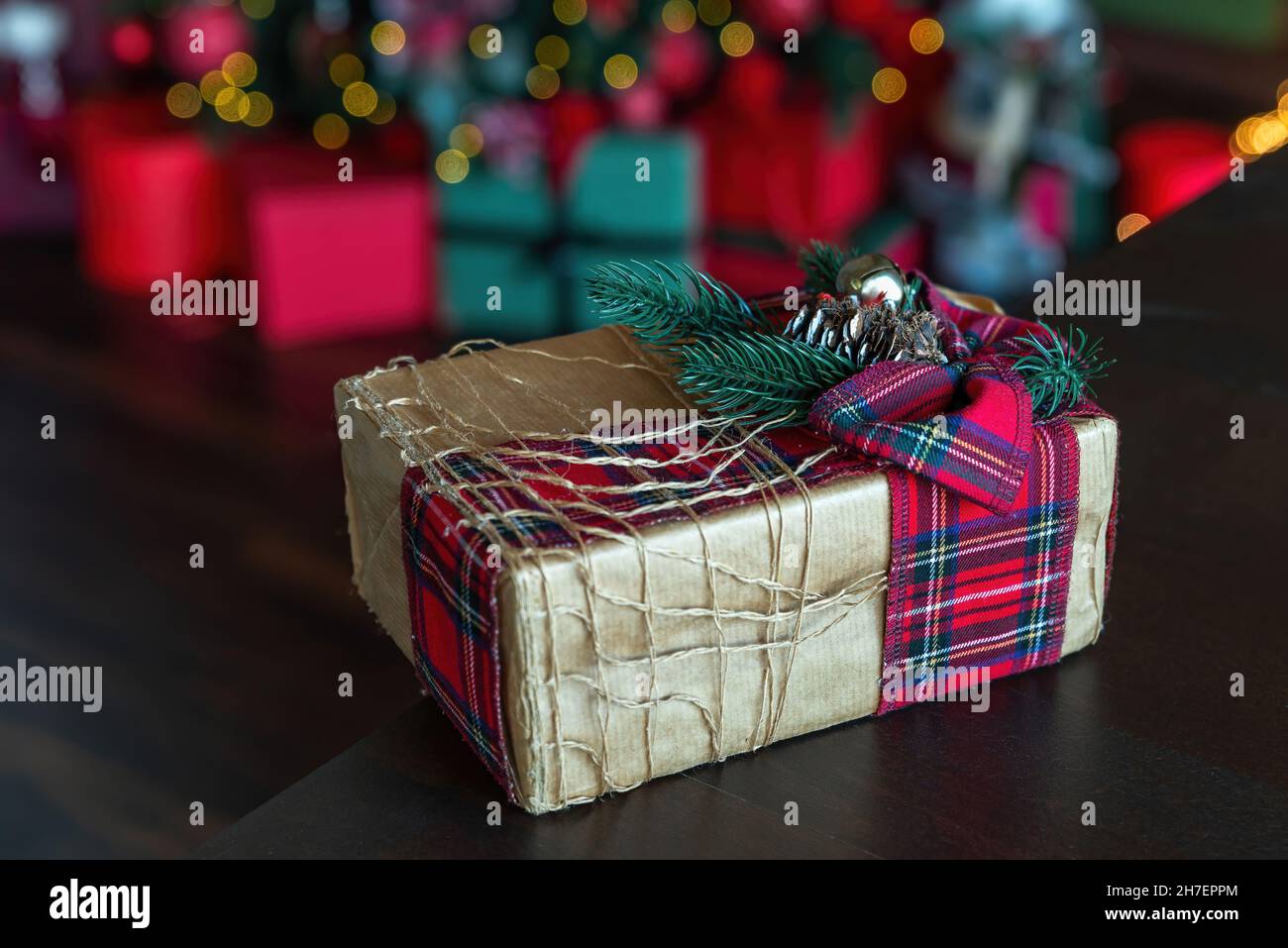Magnifique boîte cadeau de noël enveloppée de papier artisanal et attachée avec un ruban à carreaux décoré d'une branche d'épicéa.Cadeau fait maison.Des lumières de noël défocacées et un arrière-plan de présentation. Banque D'Images