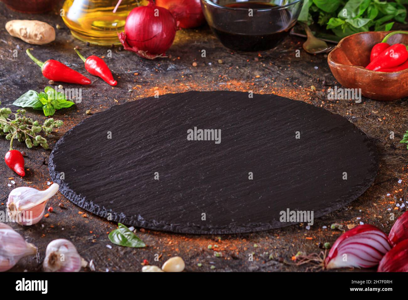 Décor culinaire avec table ronde en ardoise, huile d'olive dans une carafe et légumes.Espace vide pour le menu ou la recette avec mise au point sélective Banque D'Images