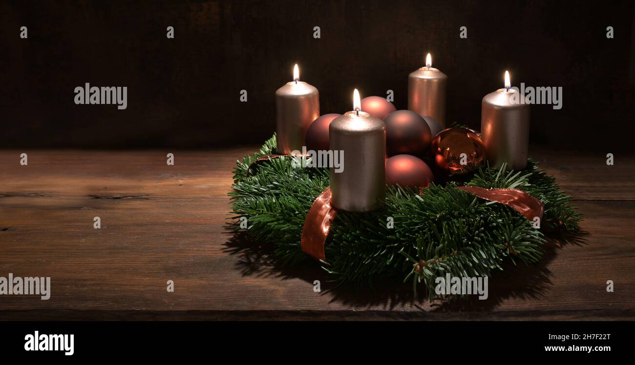 Quatrième couronne de l'Avent avec bougies couleur cuivre et boules de Noël sur une table rustique en bois sur fond brun foncé, panoramique Banque D'Images