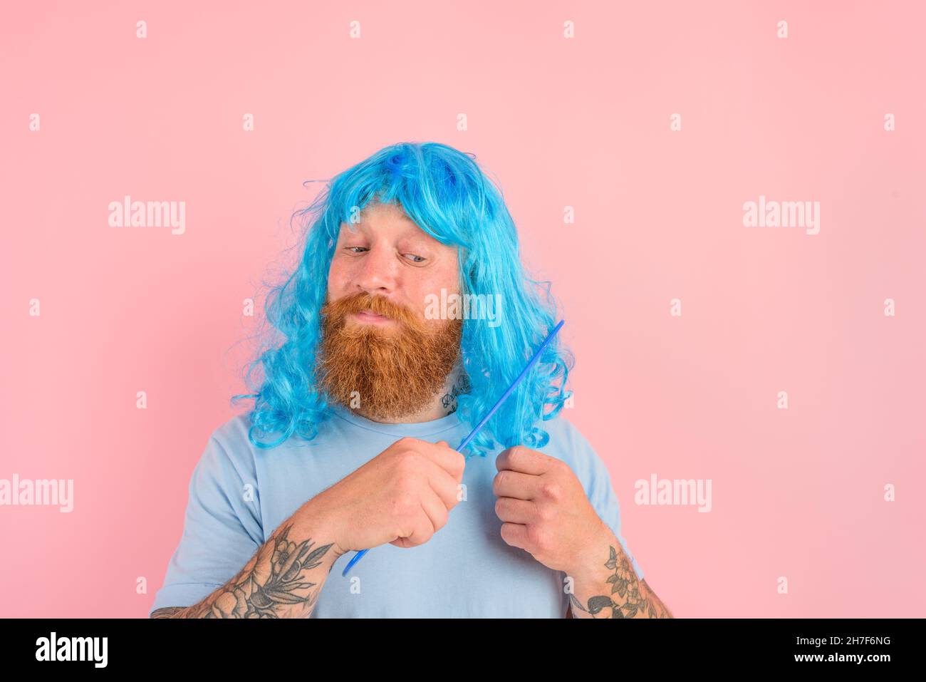 Homme attentionné avec barbe et peruke bleu peigne ses cheveux comme une femme Banque D'Images