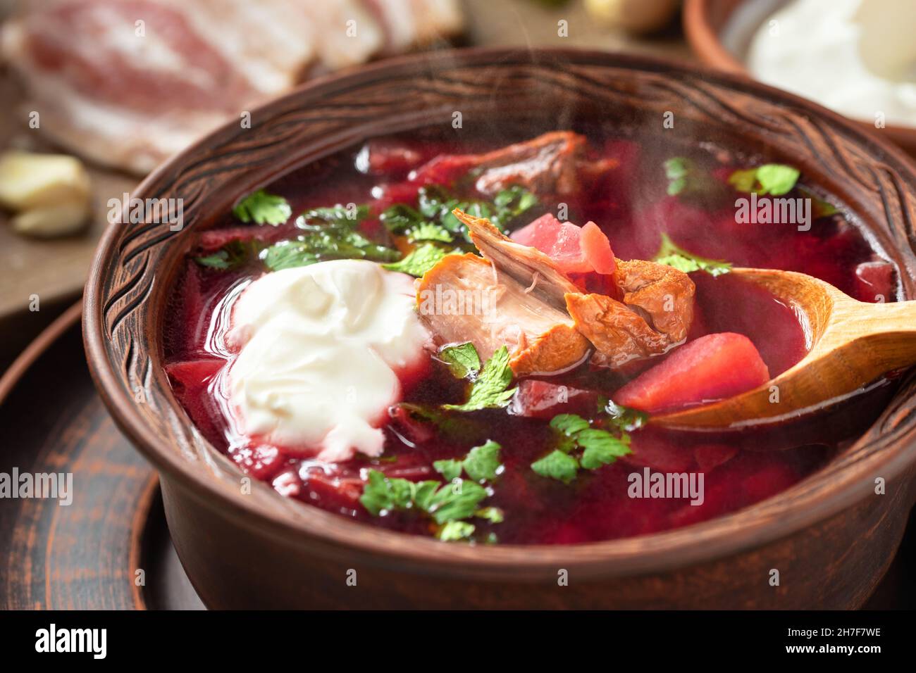 Le borscht fraîchement cuit est un plat traditionnel de cuisine russe et ukrainienne composé de plats en faïence avec bacon, pain, crème sure et ail. Banque D'Images