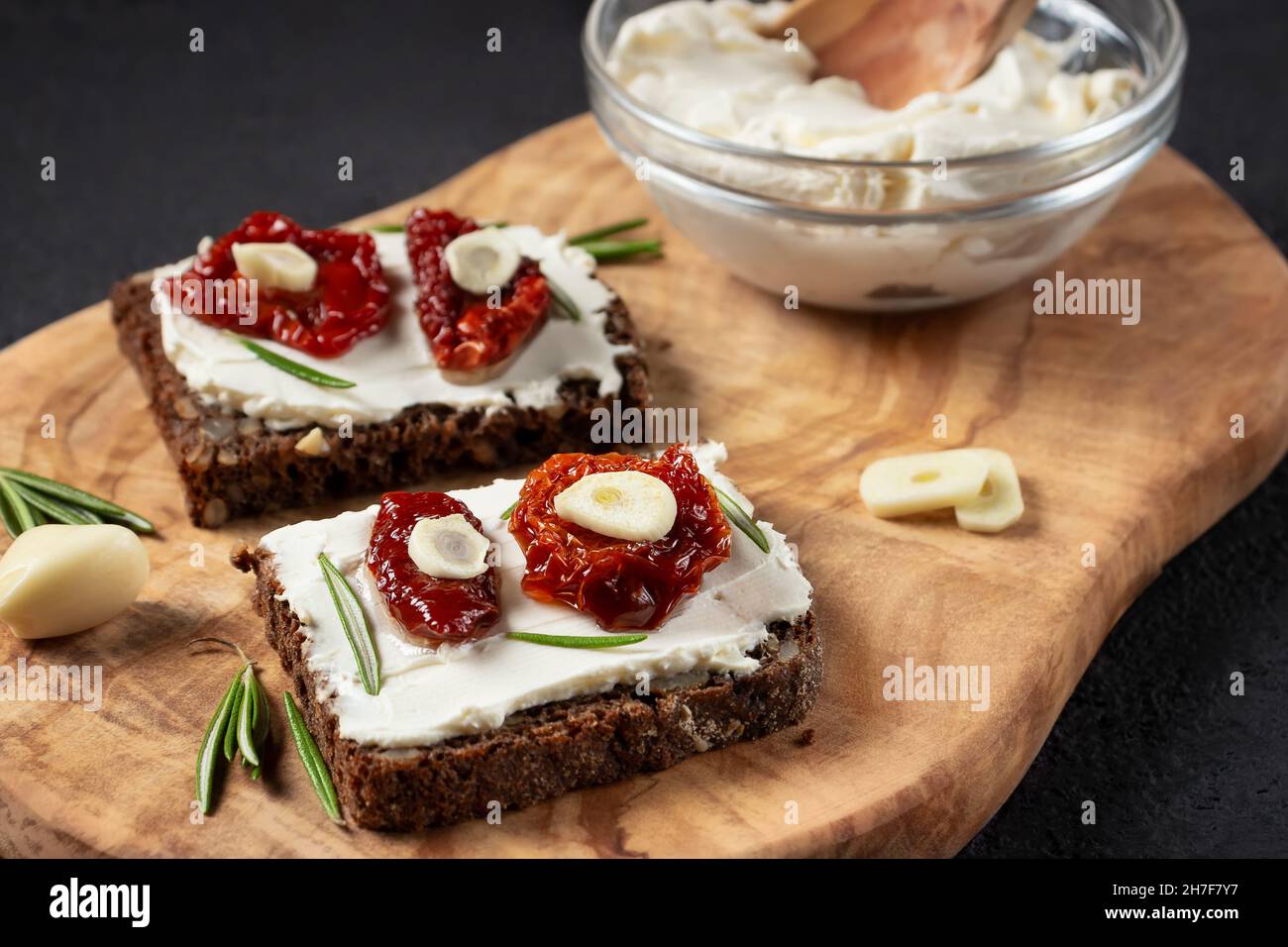 Des sandwichs au pain multigrain faits maison avec fromage à la crème et tomates séchées sur un plateau en bois. Concept de saine alimentation Banque D'Images