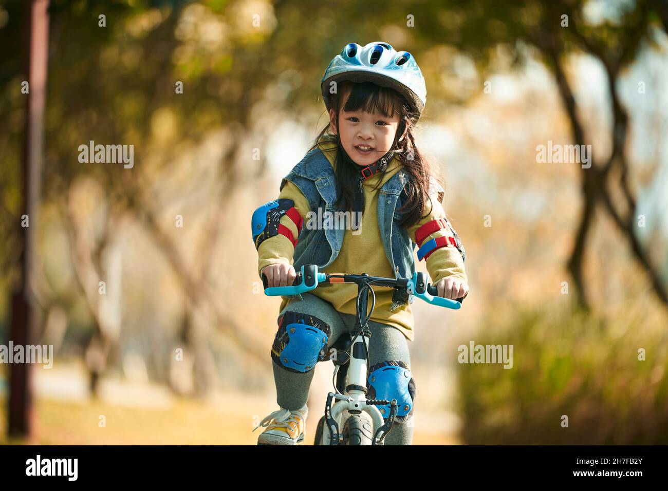 jolie petite fille asiatique heureuse avec casque et équipement de protection complet à vélo dans le parc de la ville Banque D'Images