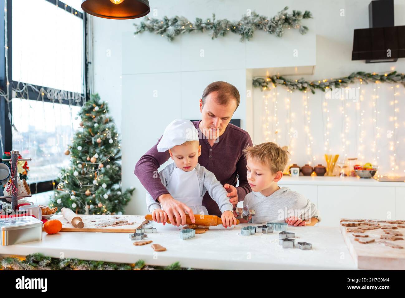Père avec deux enfants cuisiner faire du pain d'épice, couper des biscuits de pâte de pain d'épice, s'amuser.Repas de fête, processus de cuisson, cuisine familiale, Chr Banque D'Images