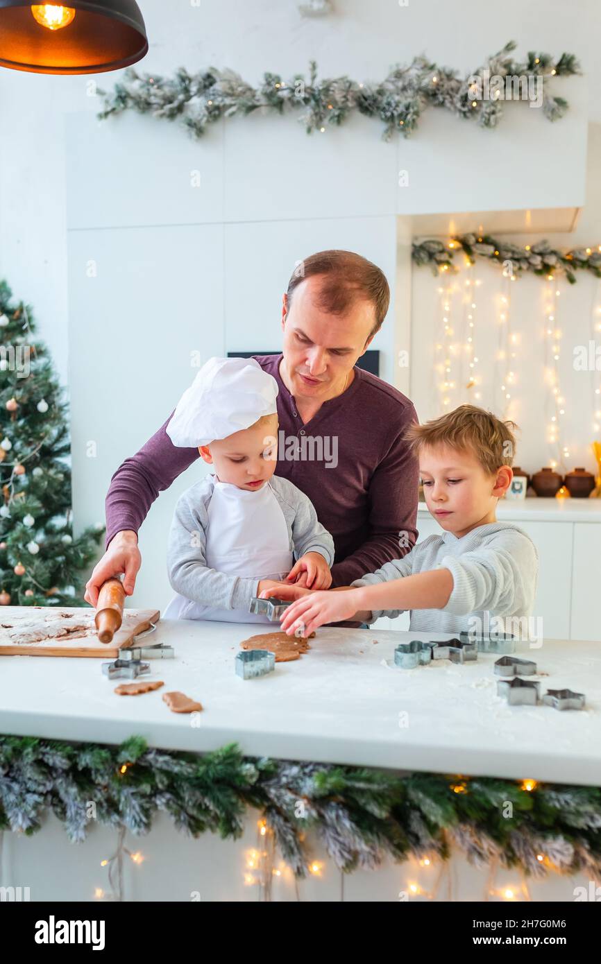 Père avec deux enfants cuisiner faire du pain d'épice, couper des biscuits de pâte de pain d'épice, s'amuser.Repas de fête, processus de cuisson, cuisine familiale, Chr Banque D'Images