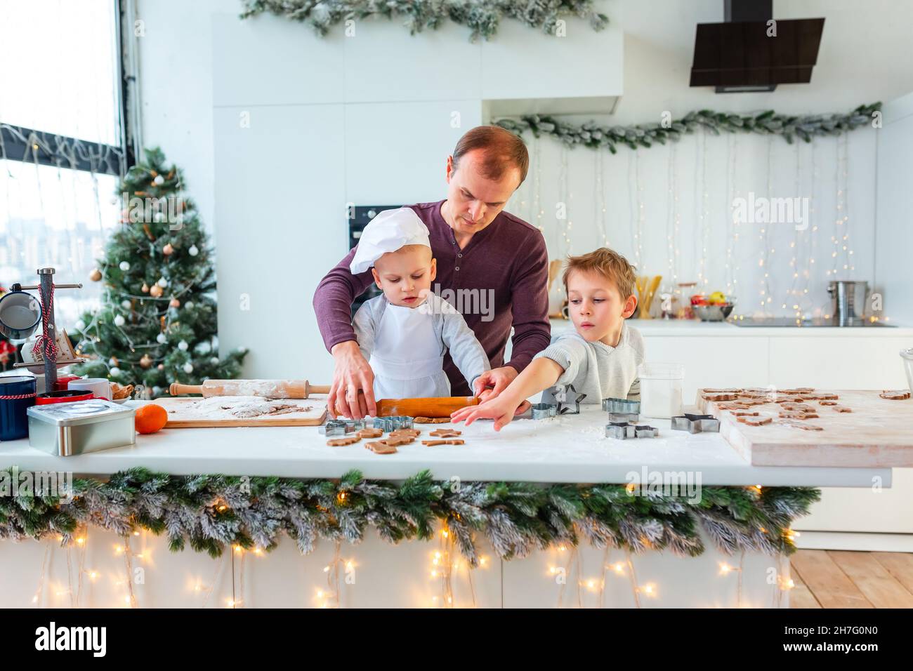 Père avec deux enfants cuisiner faire du pain d'épice, couper des biscuits de pâte de pain d'épice, s'amuser.Repas de fête, processus de cuisson, cuisine familiale, Chr Banque D'Images