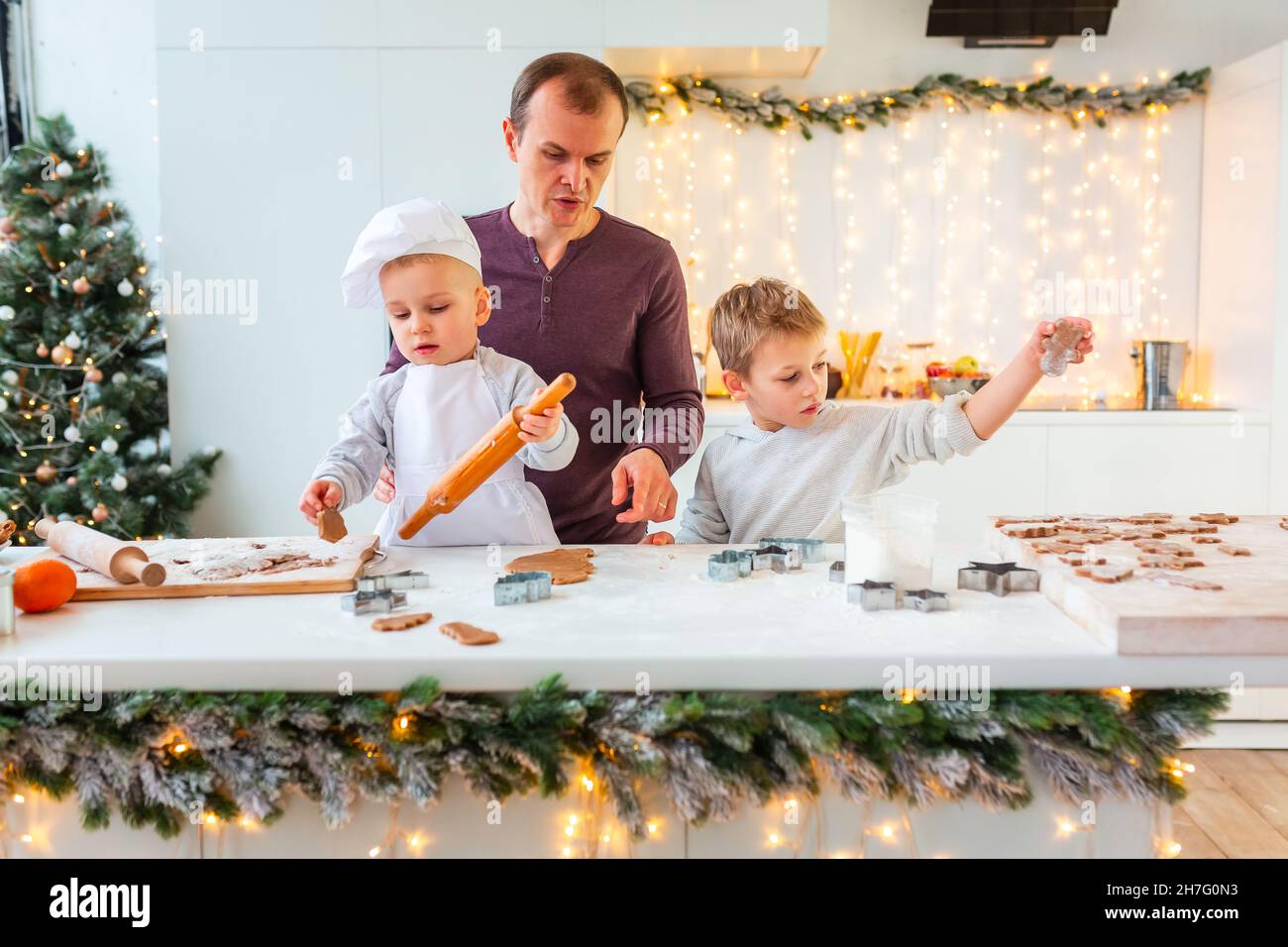 Père avec deux enfants cuisiner faire du pain d'épice, couper des biscuits de pâte de pain d'épice, s'amuser.Repas de fête, processus de cuisson, cuisine familiale, Chr Banque D'Images