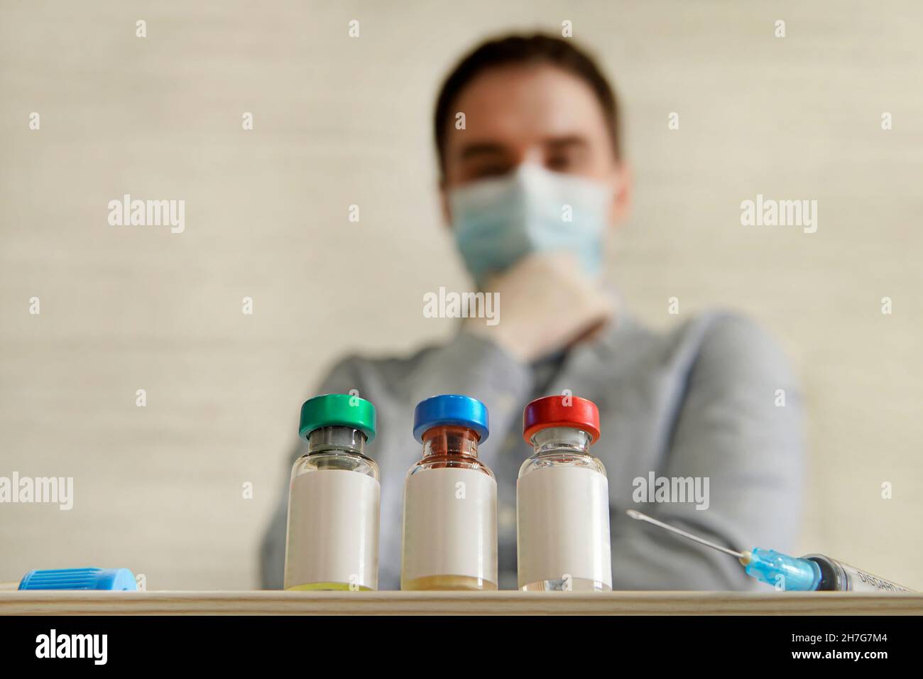 L'homme masqué regarde les bouteilles de différents vaccins, l'étiquette blanche vide sur la bouteille pour le texte et la conception.Le choix du vaccin. Banque D'Images