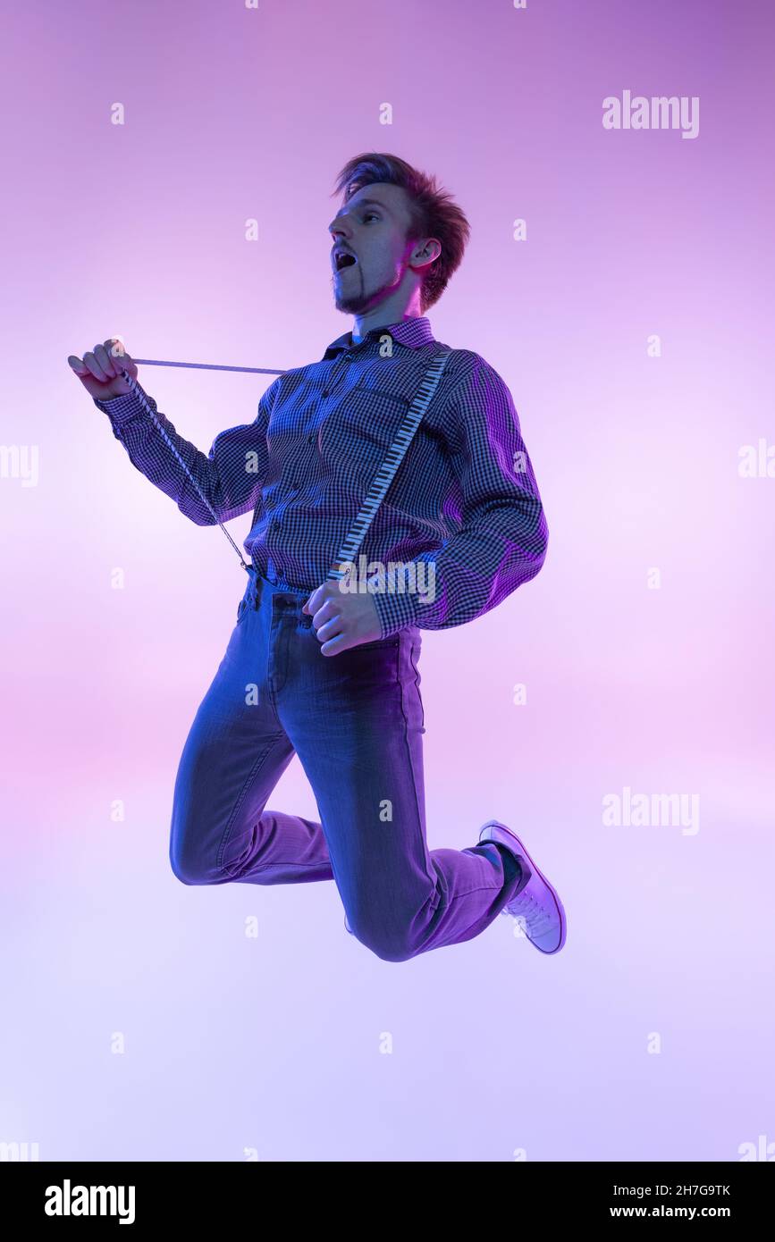 Portrait d'un jeune homme élégant en vêtements rétro vintage dansant swing dance isolée sur fond de couleur lilas dans la lumière néon Banque D'Images