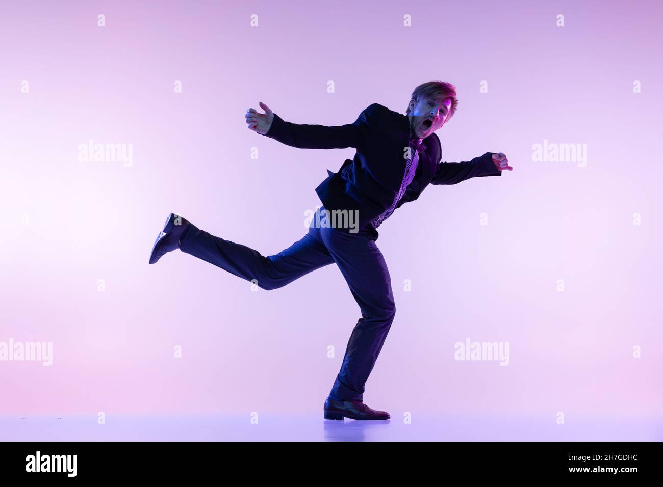 Portrait d'un jeune homme élégant en vêtements rétro vintage dansant swing dance isolée sur fond de couleur lilas dans la lumière néon Banque D'Images