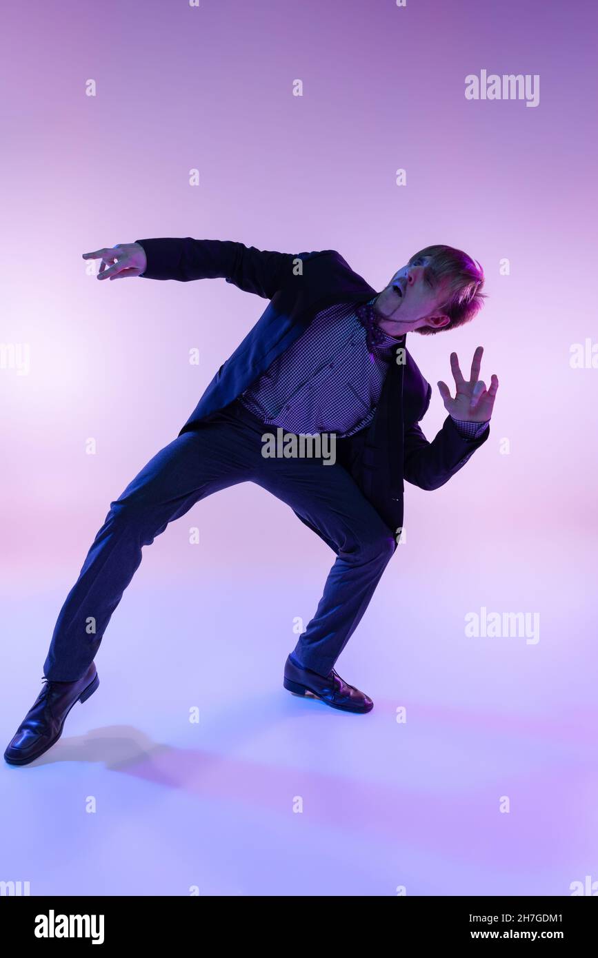 Portrait en gros plan d'un jeune homme élégant dans des vêtements rétro vintage dansant swing dance isolée sur fond de couleur lilas dans la lumière néon Banque D'Images