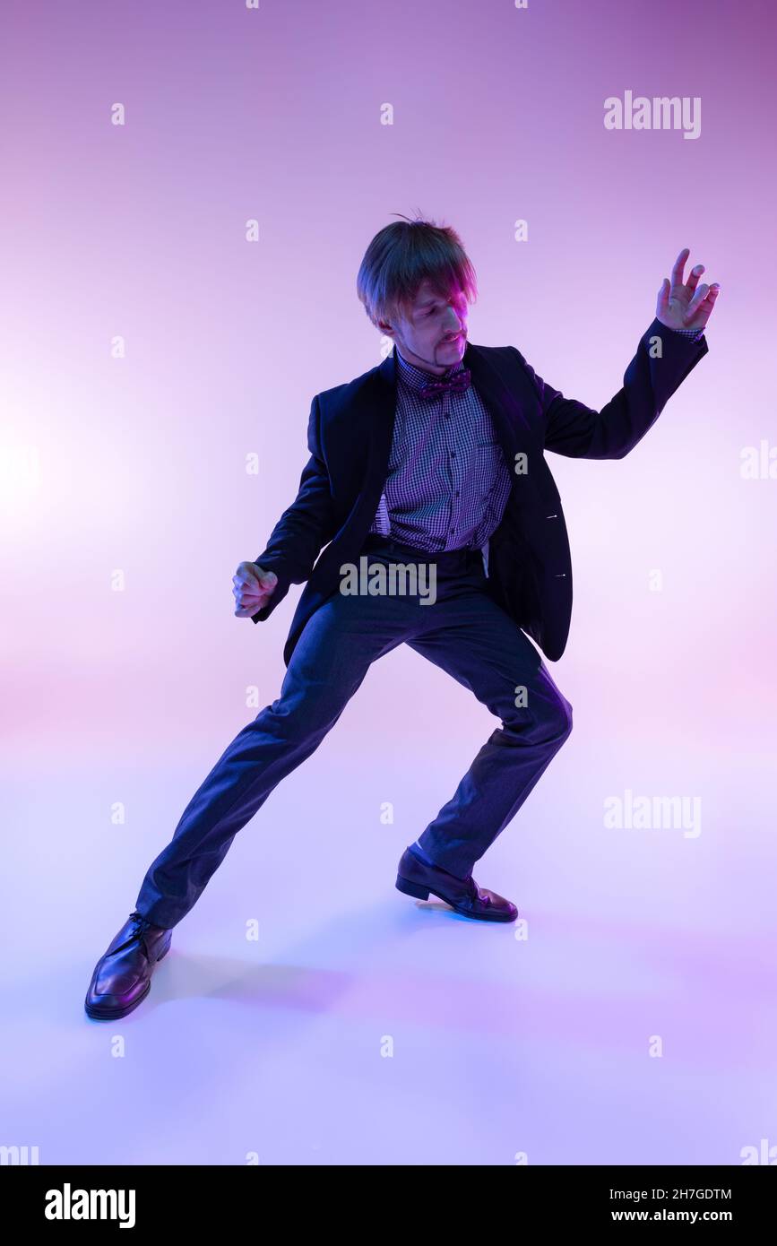 Portrait en gros plan d'un jeune homme élégant dans des vêtements rétro vintage dansant swing dance isolée sur fond de couleur lilas dans la lumière néon Banque D'Images