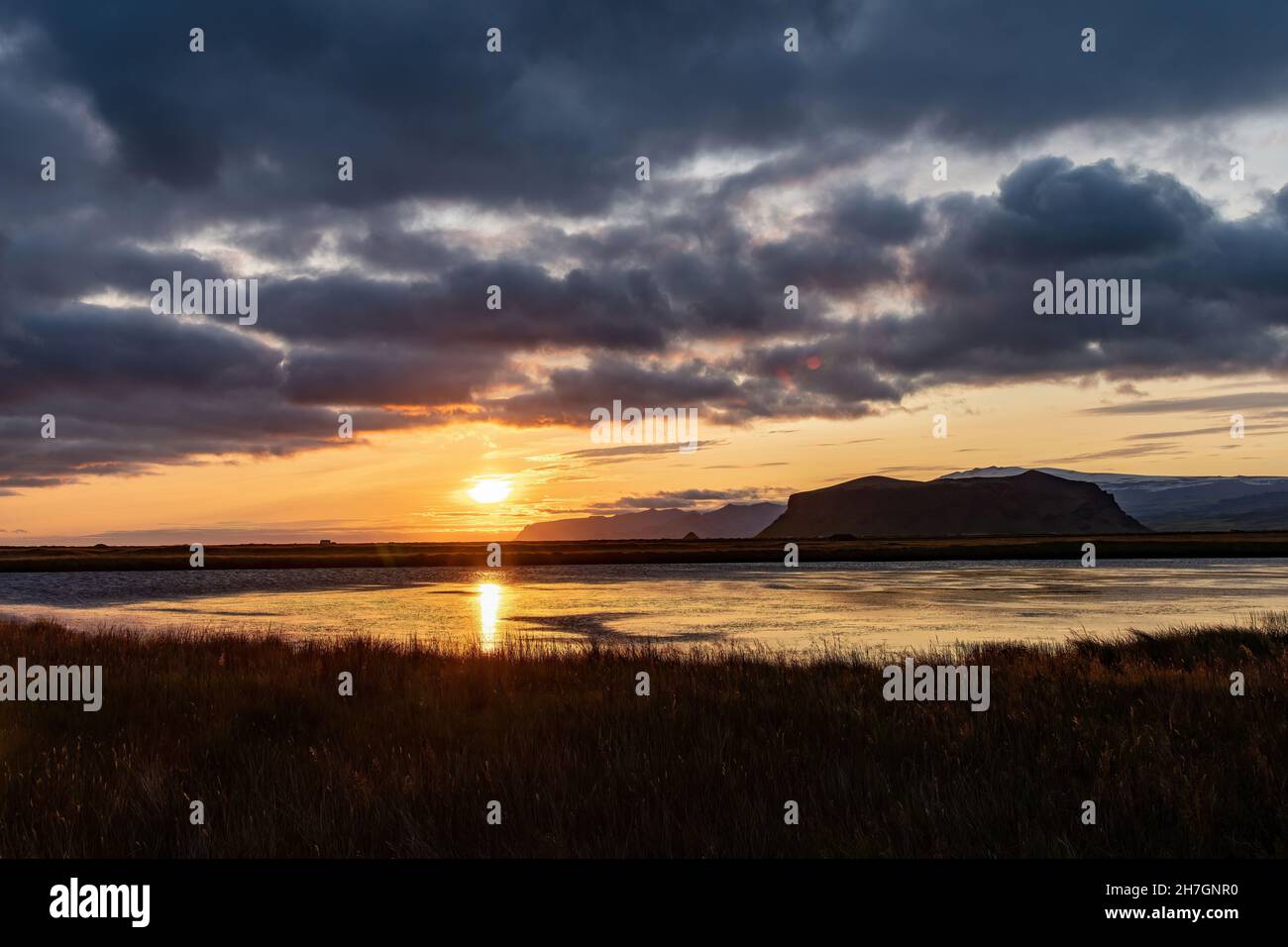 Vue panoramique le long de la côte d'Islande au coucher du soleil avec de grandes formations rocheuses dans l'océan et des nuages sombres dans le ciel Banque D'Images