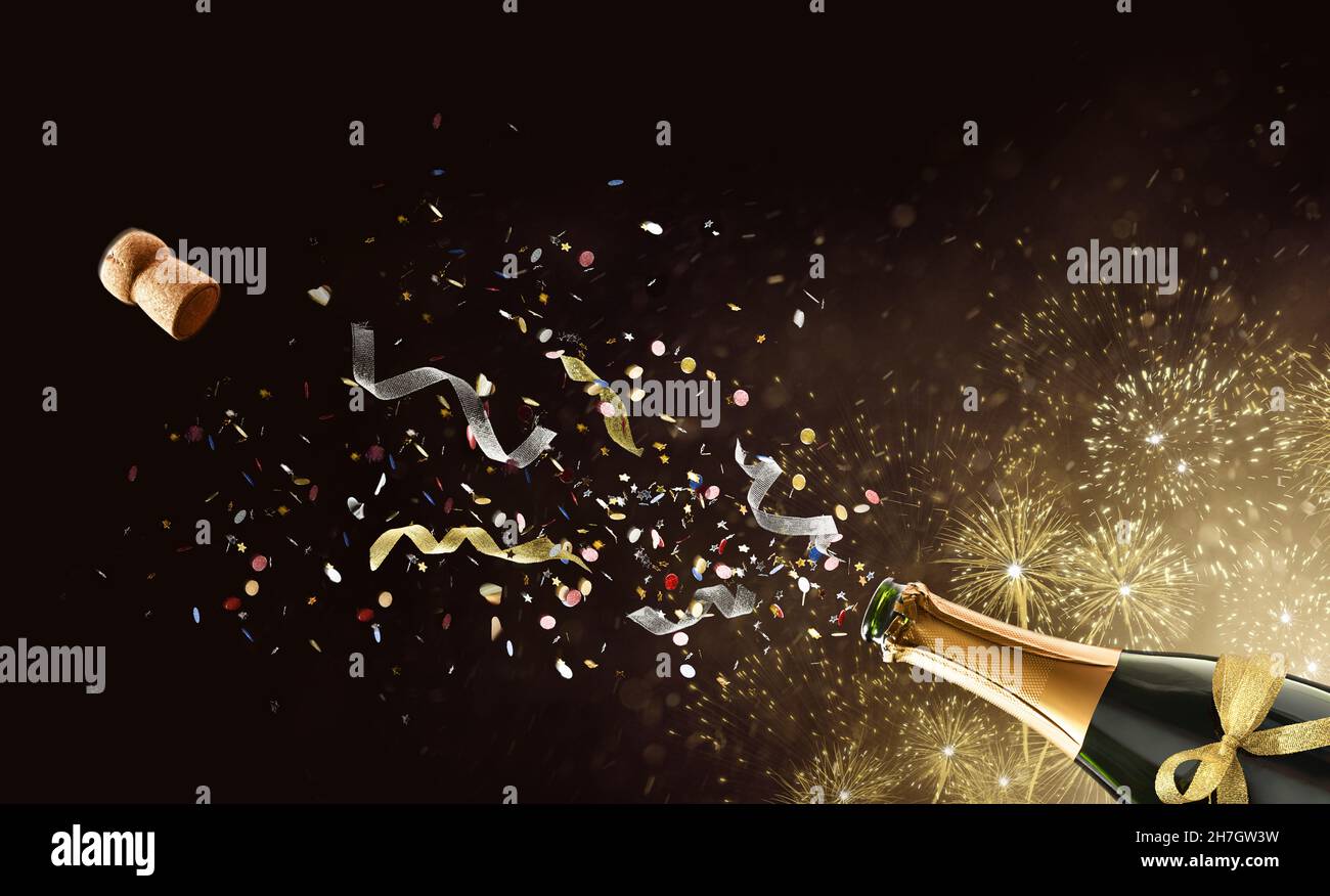 Concept festif avec une bouteille de vin pétillant fraîchement ouverte avec des confettis et des rubans sortis sur fond doré isolé avec des feux d'artifice Banque D'Images