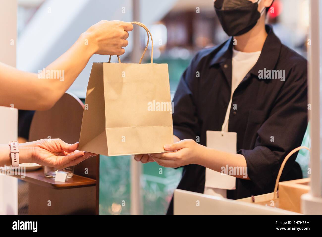 Le propriétaire de la boulangerie asiatique porte un masque de visage donnant un sac de nourriture à emporter au client Banque D'Images