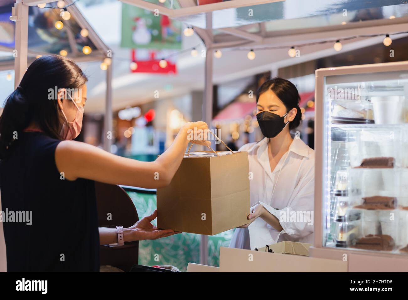Le propriétaire de la boulangerie asiatique porte un masque de visage donnant un sac de nourriture à emporter au client Banque D'Images