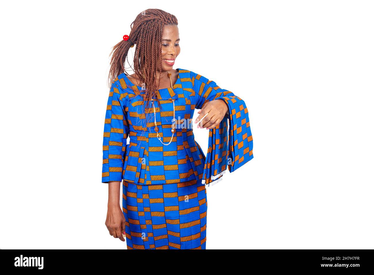 belle femme d'affaires africaine en robe traditionnelle debout sur fond blanc regardant pour voir son tissu tout en souriant Banque D'Images