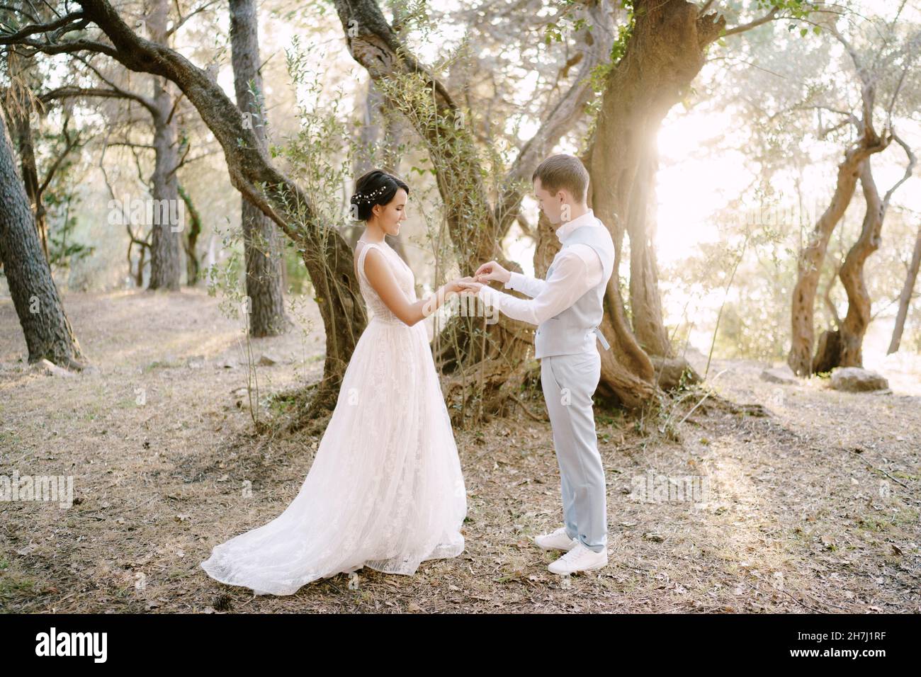 Marié met l'anneau de mariage sur le doigt de la mariée parmi les arbres dans l'oliveraie Banque D'Images