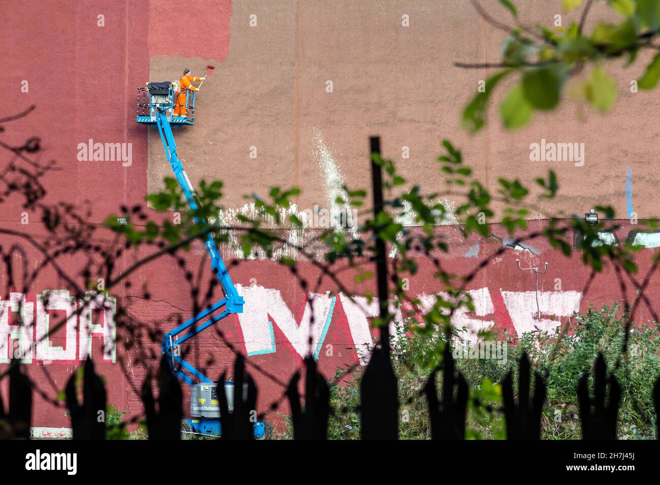 Un homme sur un préparateur de cerise peint un mur pour couvrir le graffiti, Glasgow, Écosse, Royaume-Uni Banque D'Images