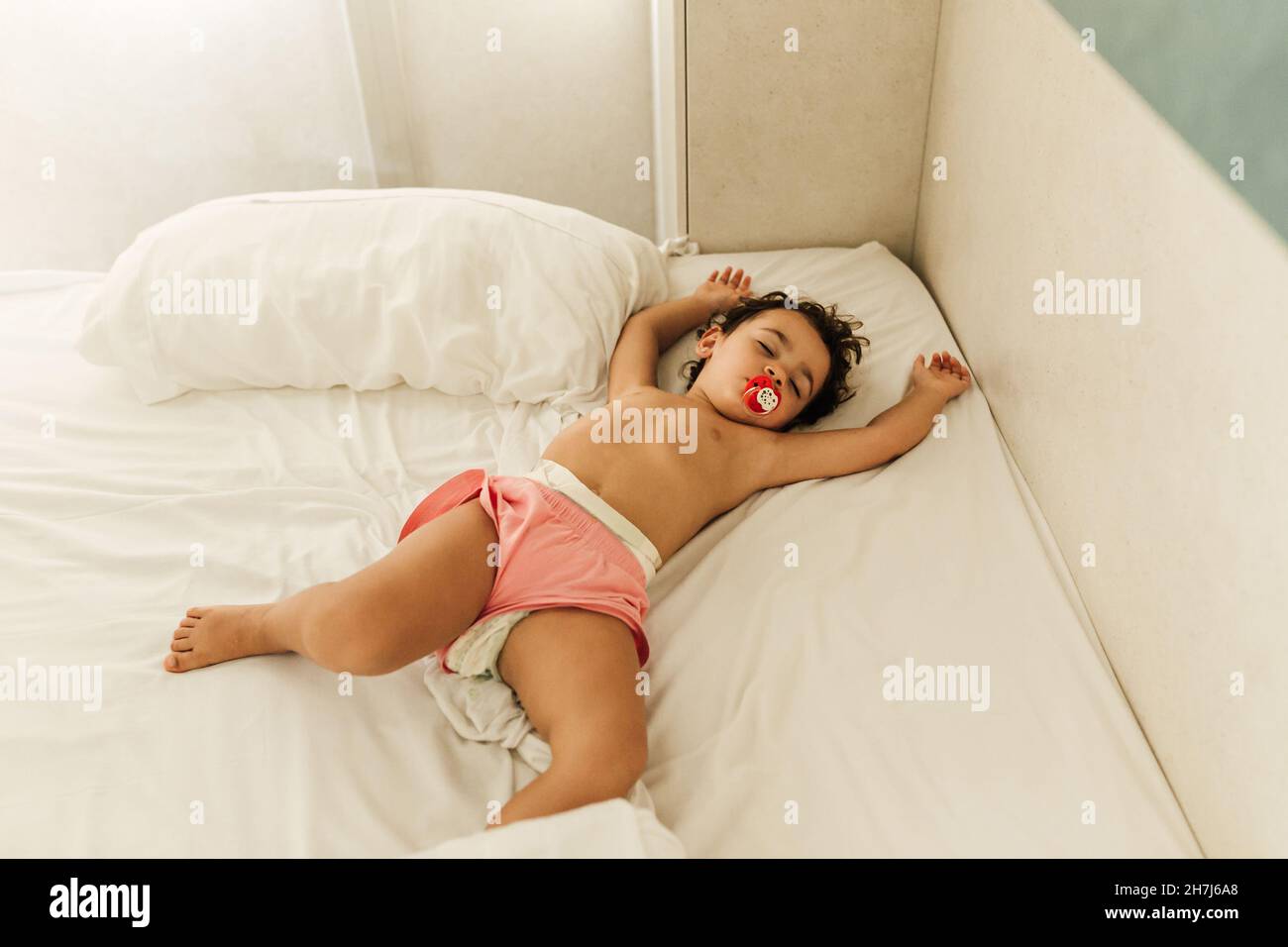 Petite fille mignonne avec une sucette dormant confortablement dans un lit. Banque D'Images