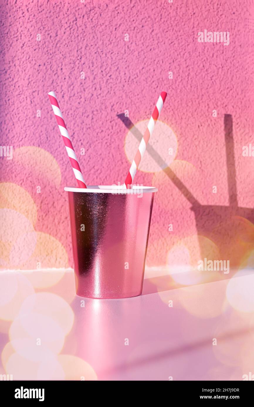 Gobelet jetable rose avec paille sur la table contre le mur avec ombre, gros plan et bokeh Banque D'Images