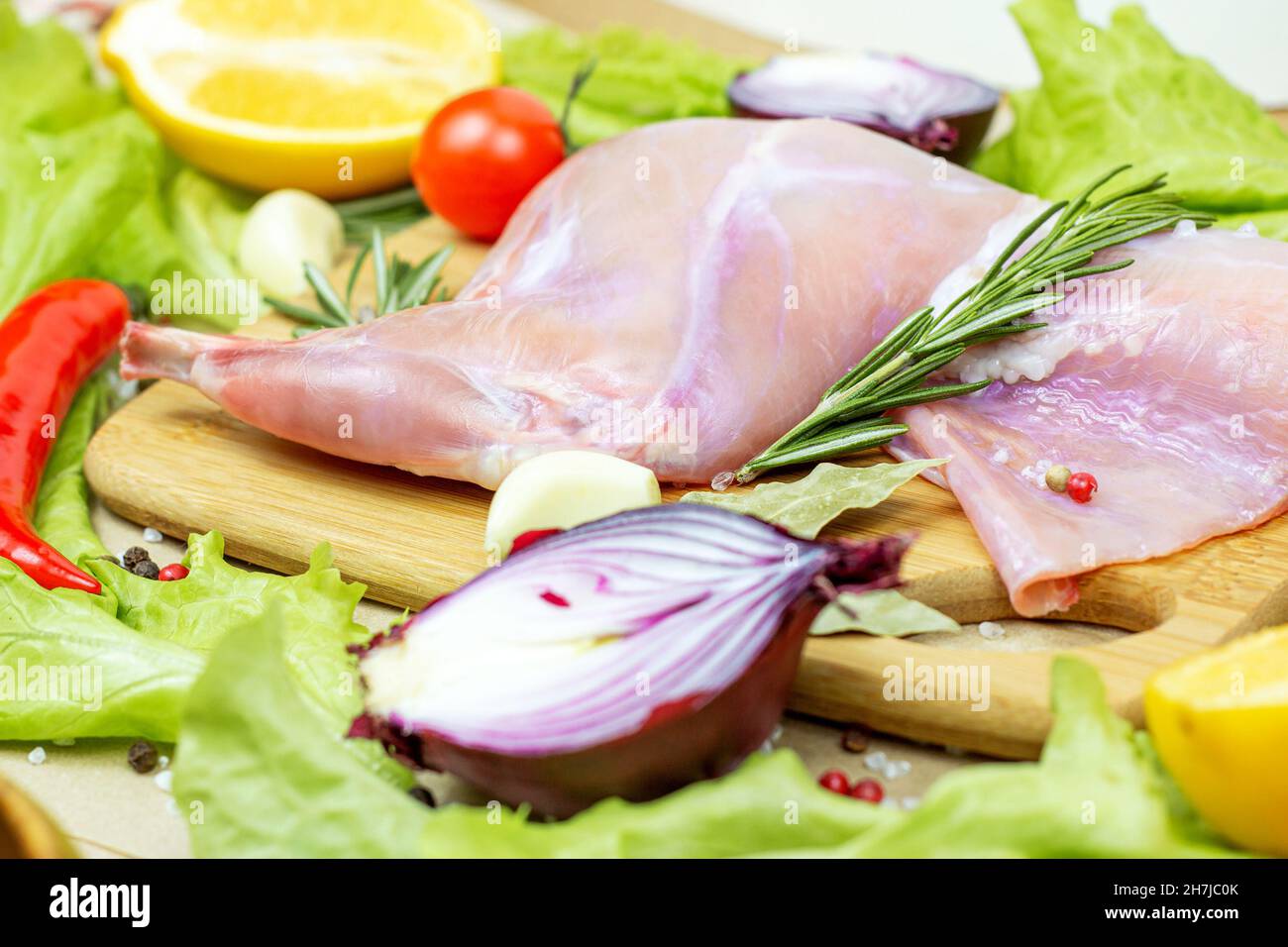 Viande de lapin rose cru non cuite avec romarin vert et légumes frais sur fond de planche à découper en bois clair. Banque D'Images