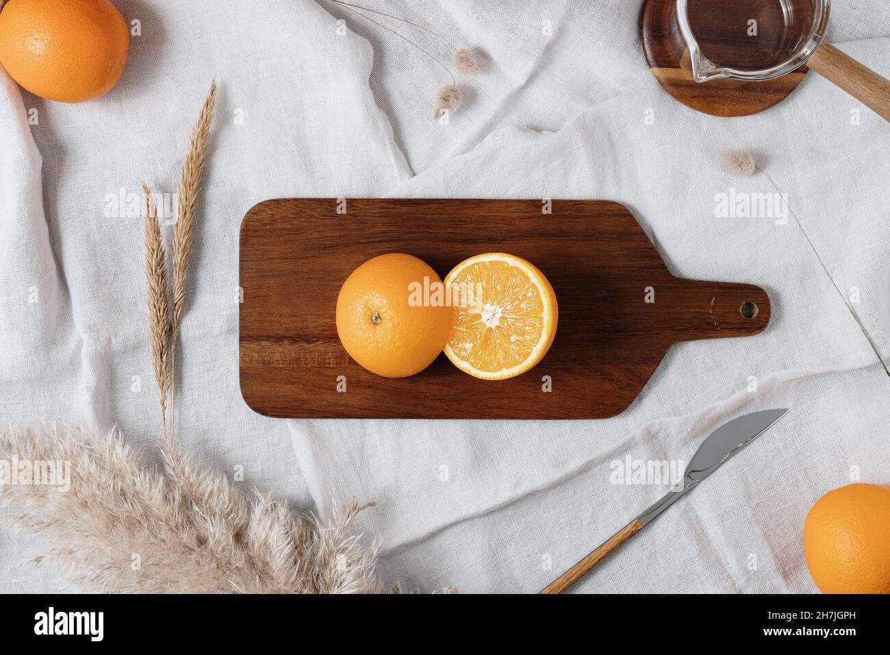 Deux demi-oranges sur une planche à découper en bois marron entourée d'un couteau, d'une tasse à verser et de fleurs séchées et d'oranges entières.Idée de petit déjeuner sain. Banque D'Images