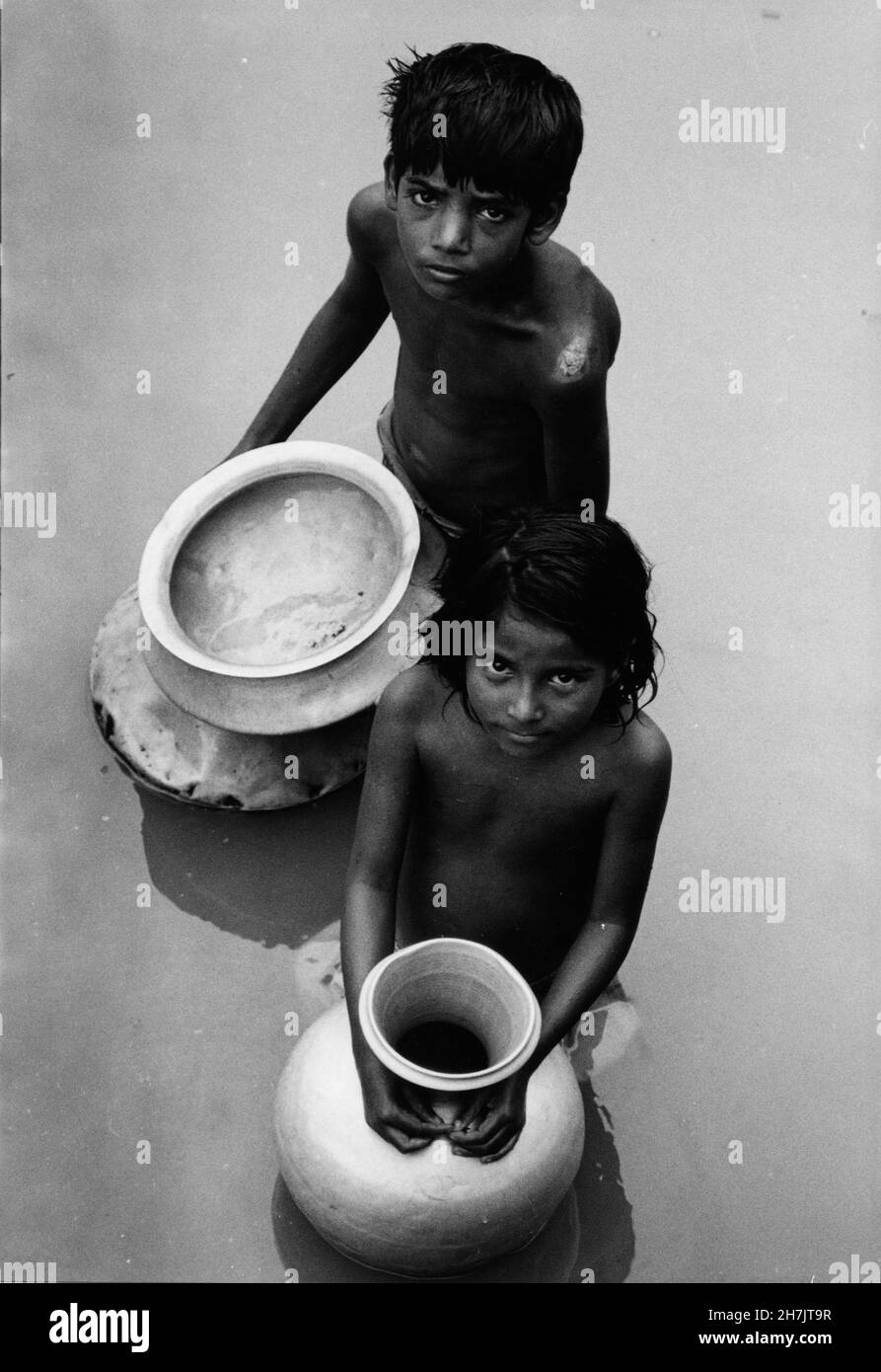 Un jeune garçon et une fille portent des pots vides, à la recherche d'eau potable, au milieu de l'une des pires inondations que le Bangladesh ait jamais connu en 1988, en D. Banque D'Images