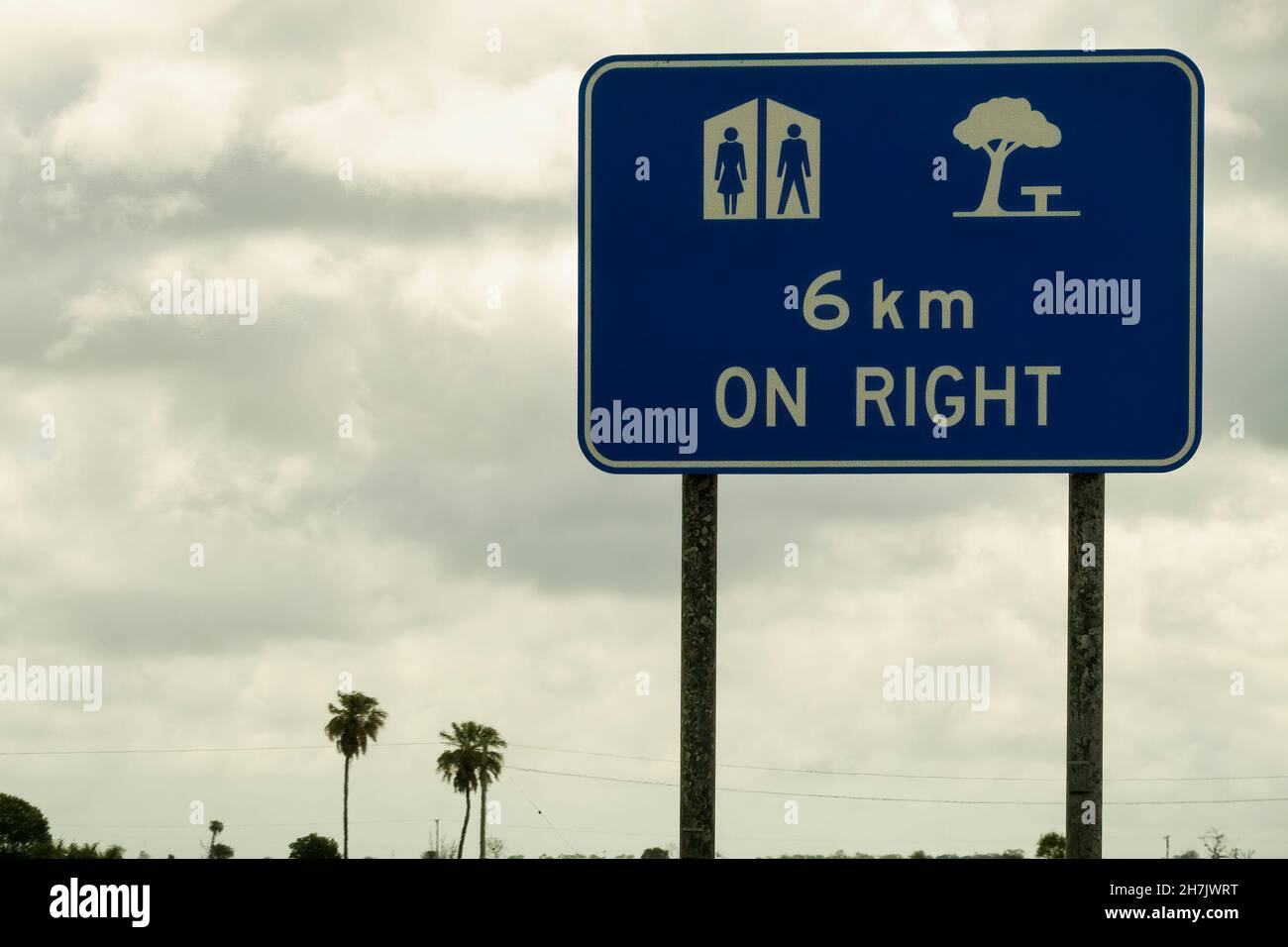 Toilettes et aire de repos devant le panneau droit sur la route contre un ciel nuageux par temps humide et pluvieux Banque D'Images