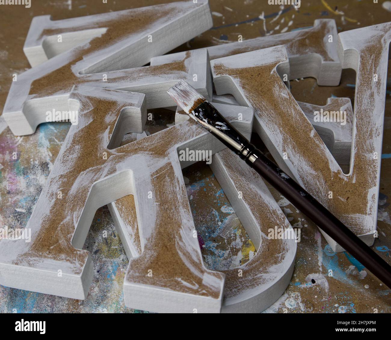 Diverses lettres non finies et non peintes en MDF sur une table d'atelier avec un pinceau Banque D'Images