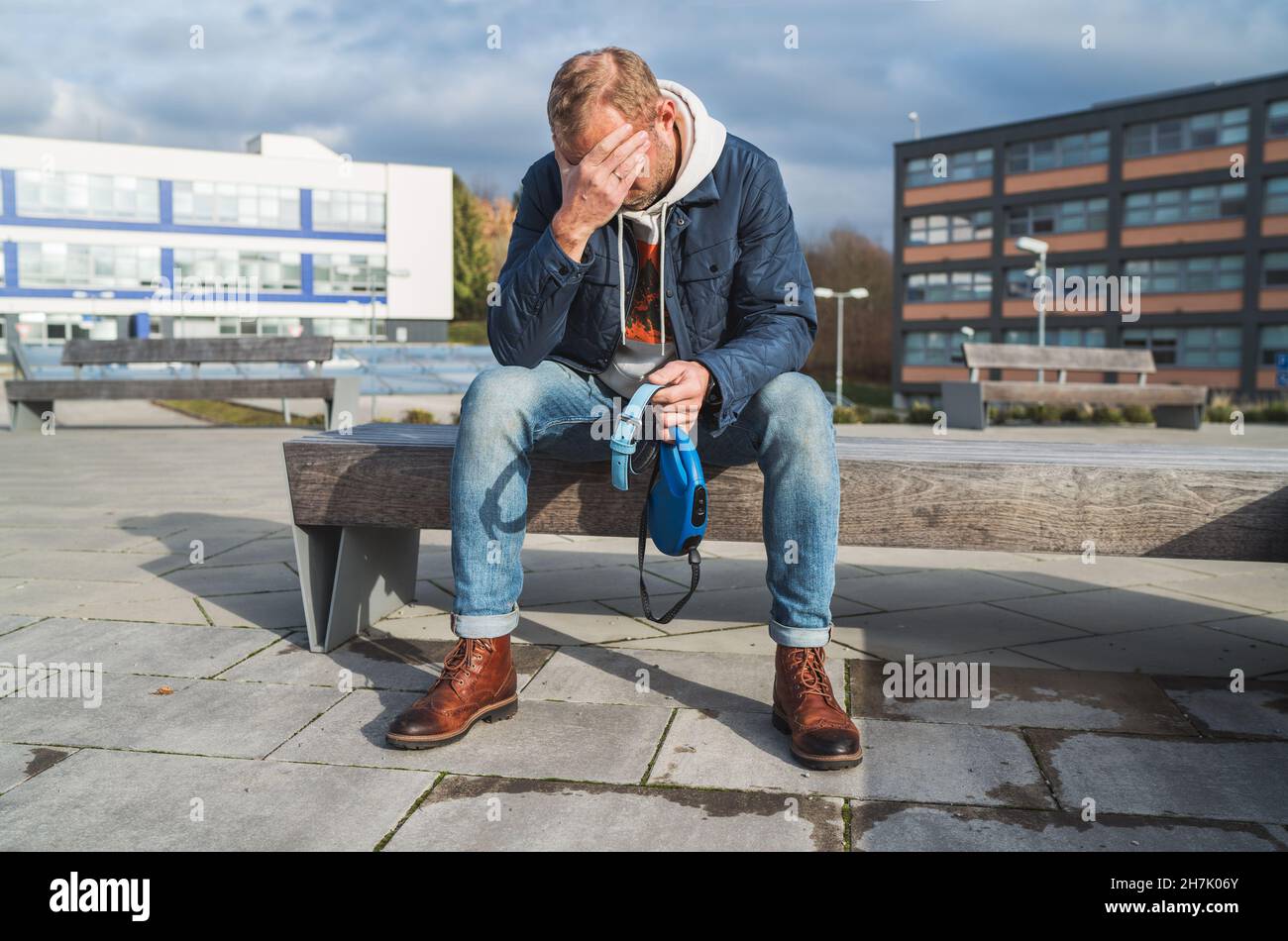 Cassé avec le chagrin d'homme comme un propriétaire de chien est en train de pleurer assis sur un banc avec le collier d'animal de compagnie et la laisse, pleurant profondément au sujet de la perte d'animal Banque D'Images