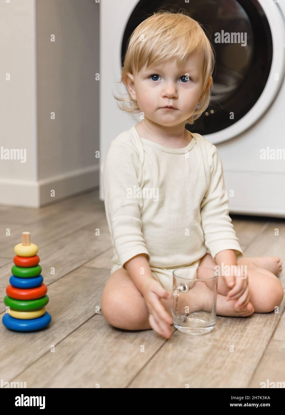 Une belle petite fille est assise sur le sol de la maison et joue avec une pyramide de jouets en bois d'anneaux colorés.Enseignement à domicile et intellectuel Banque D'Images