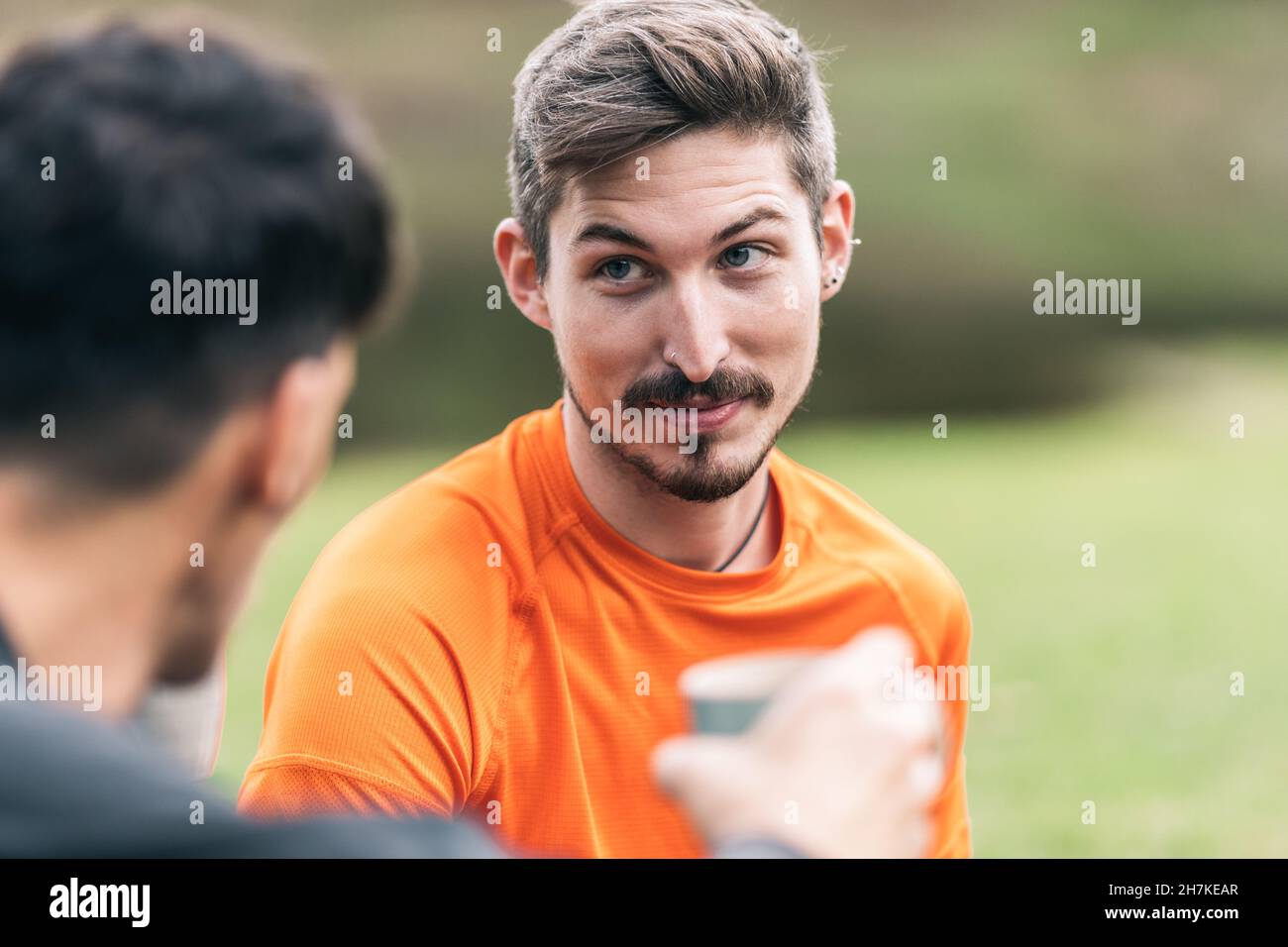 Le visage heureux d'un homme sportif qui boit du thé avec d'autres personnes dans un parc Banque D'Images
