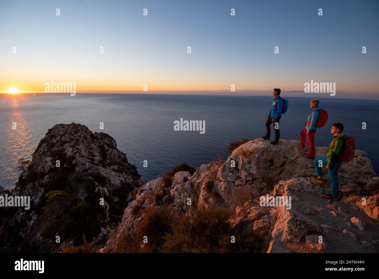 Trois randonneurs se tiennent au sommet au-dessus de la mer méditerranée et des collines et regardent, Calpe, province d'Alicante, Espagne Banque D'Images
