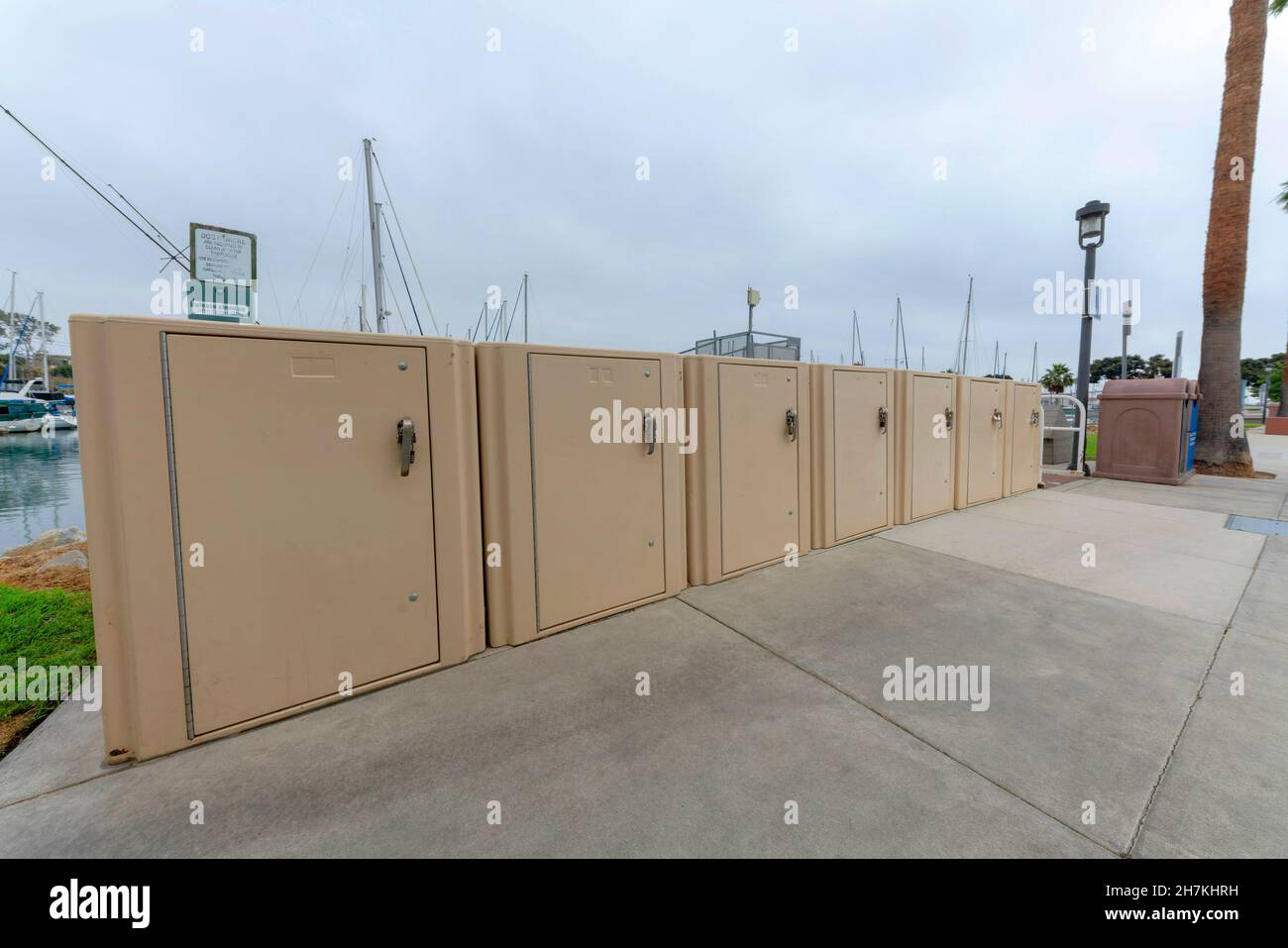 Casiers de stockage public beige à Oceanside en Californie.Des casiers publics près du trashcan et de l'arbre sur la droite contre le port et le ciel à l'arrière Banque D'Images