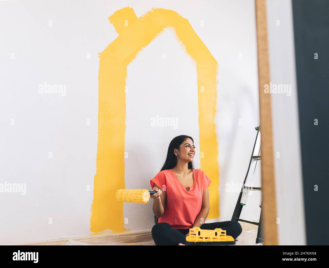 Smiling young woman painting wall at home Banque D'Images