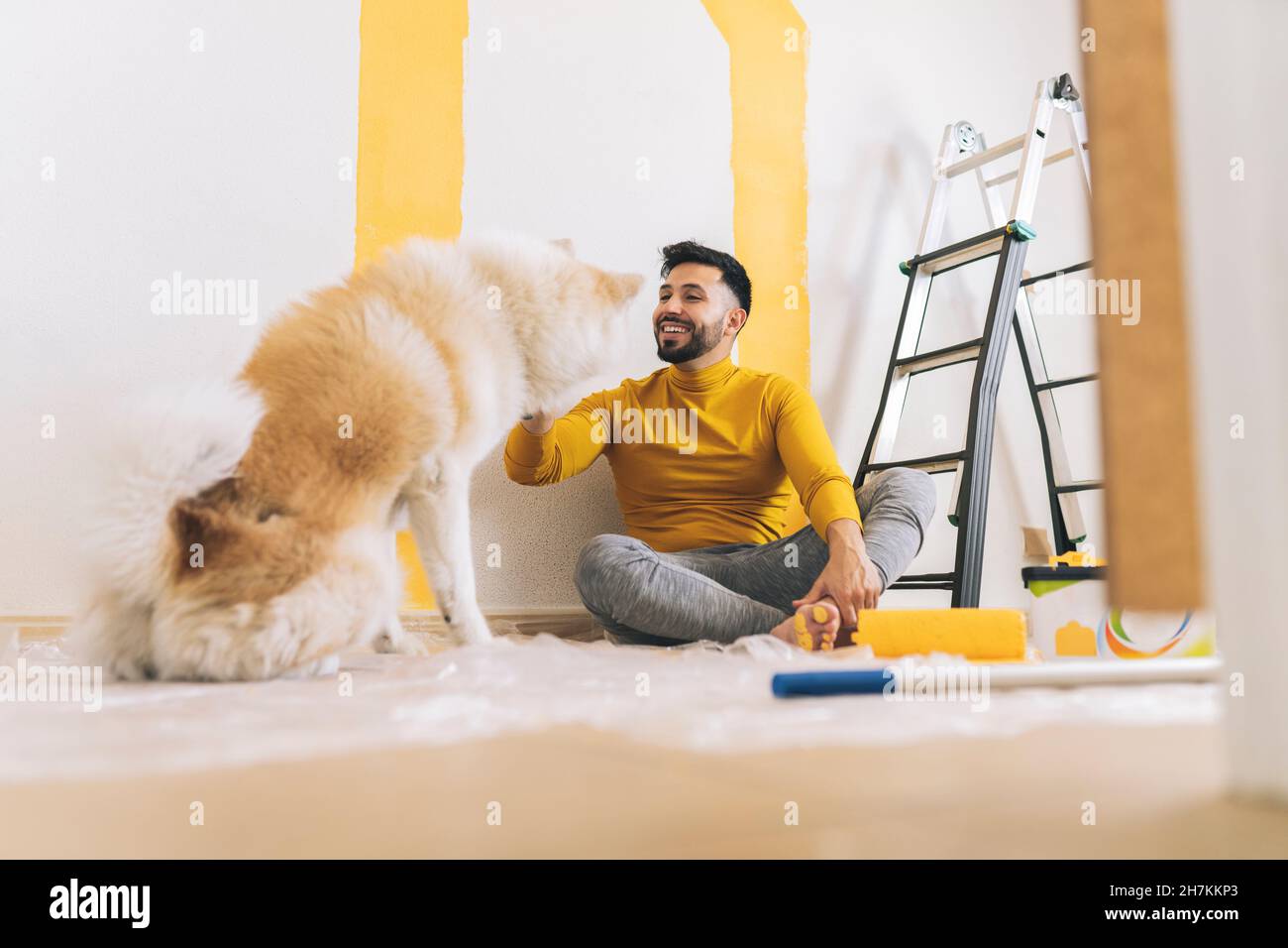 Joyeux homme beau avec de la peinture jaune à pied assis à la maison Banque D'Images