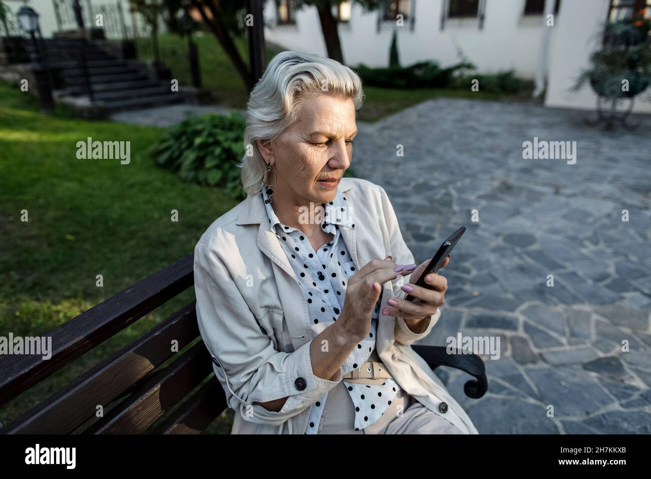 Femme âgée utilisant un téléphone portable assis sur un banc Banque D'Images