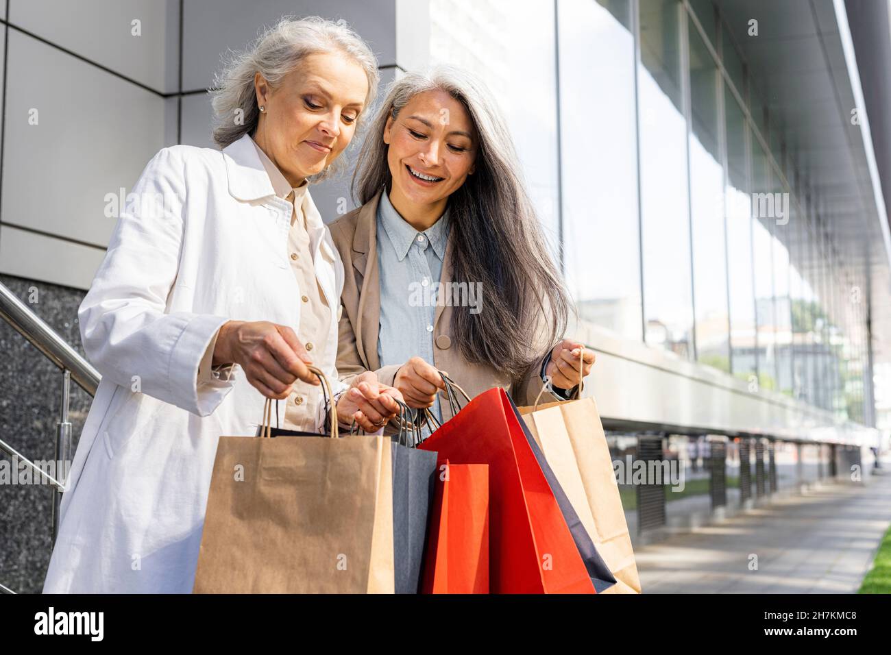 Femmes matures recherchant dans des sacs de shopping à l'extérieur du centre commercial Banque D'Images