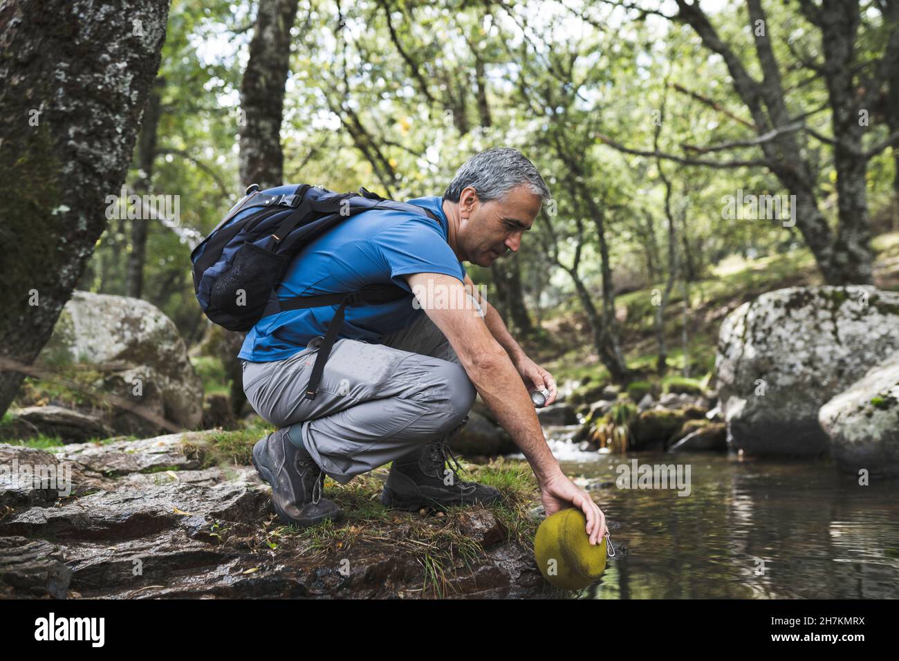 Homme mûr souriant par chien Akita dans l'eau à la forêt Banque D'Images