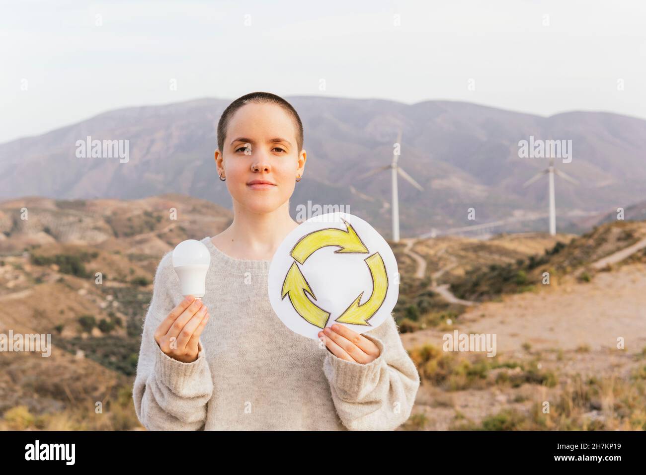 Femme tenant une ampoule et un symbole de recyclage au parc éolien Banque D'Images