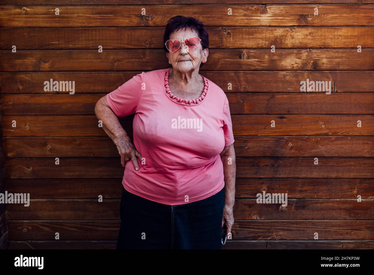 Femme âgée avec main sur la hanche debout devant un mur en bois Banque D'Images