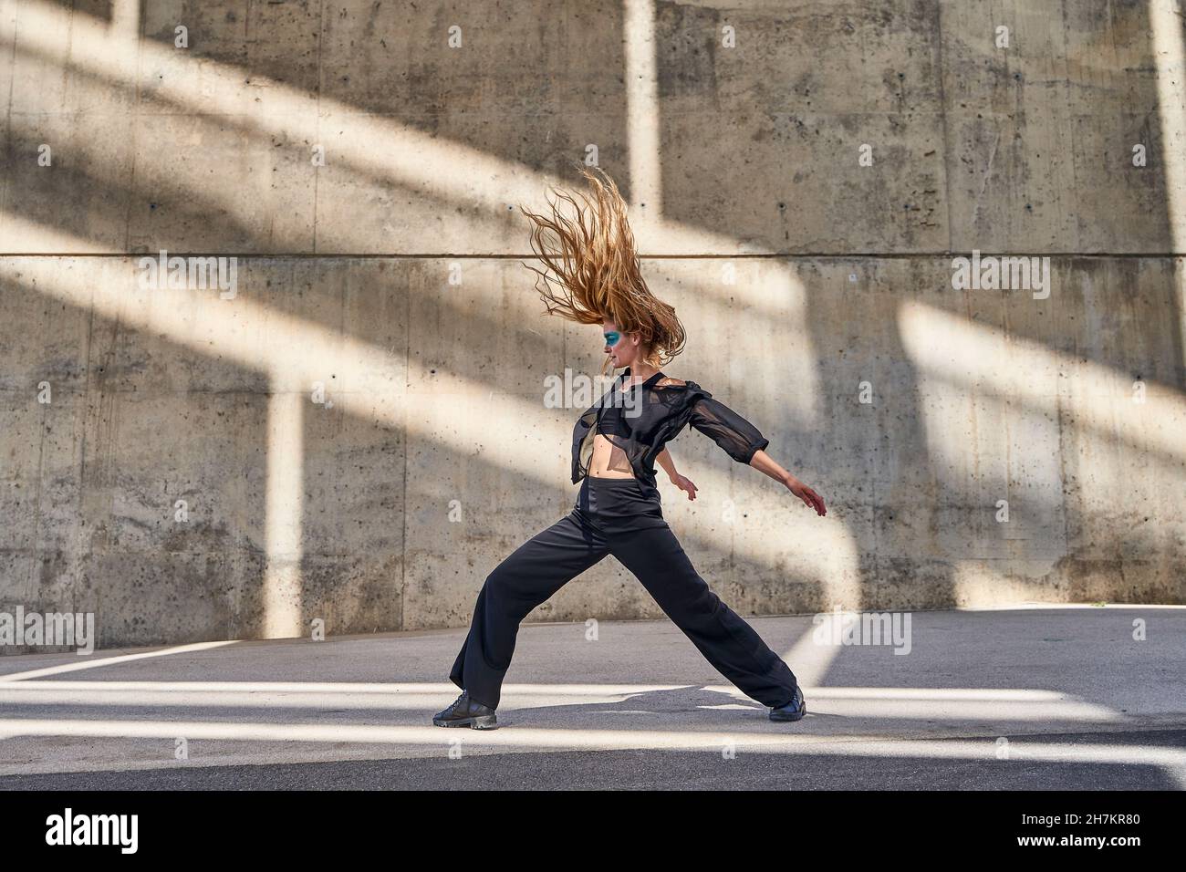 Femme avec les cheveux de jeter dansant dans la rue devant le mur Banque D'Images