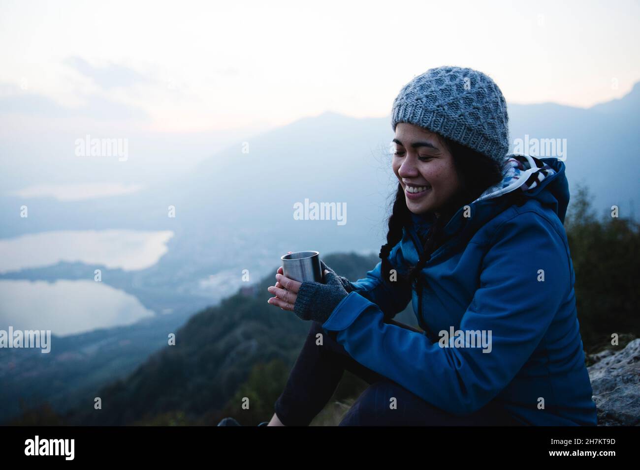 Femme souriante avec les yeux fermés tenant une tasse de café sur la montagne Banque D'Images