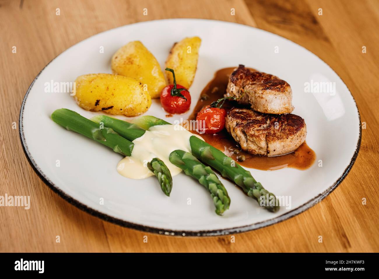 Steaks à la sauce, pommes de terre, tomates cerises cuites et tiges d'asperges Banque D'Images