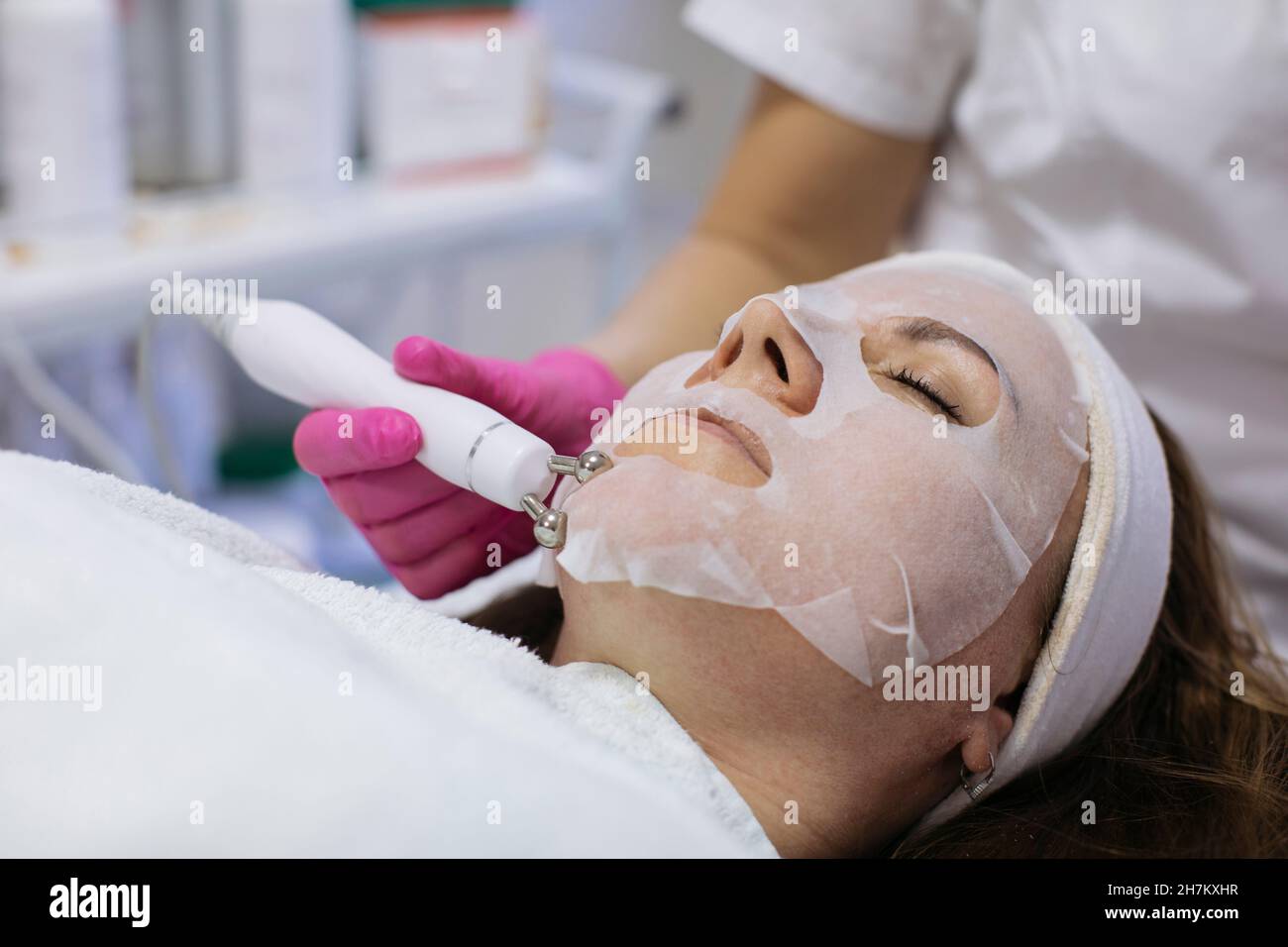Femme avec masque de feuille obtenant un traitement de beauté en salon Banque D'Images