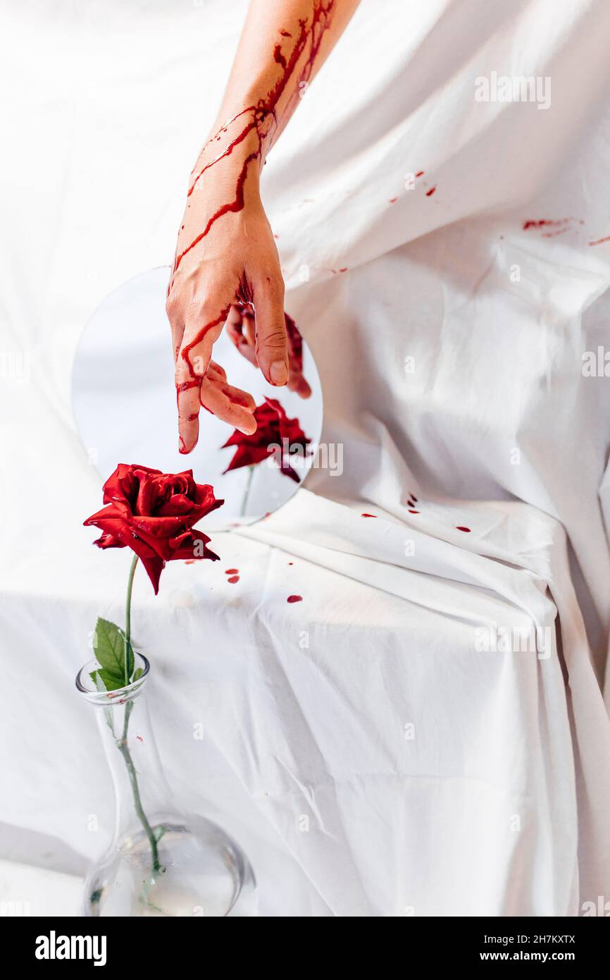 Femme avec main sanglante touchant rouge rose dans vase de fleur Banque D'Images