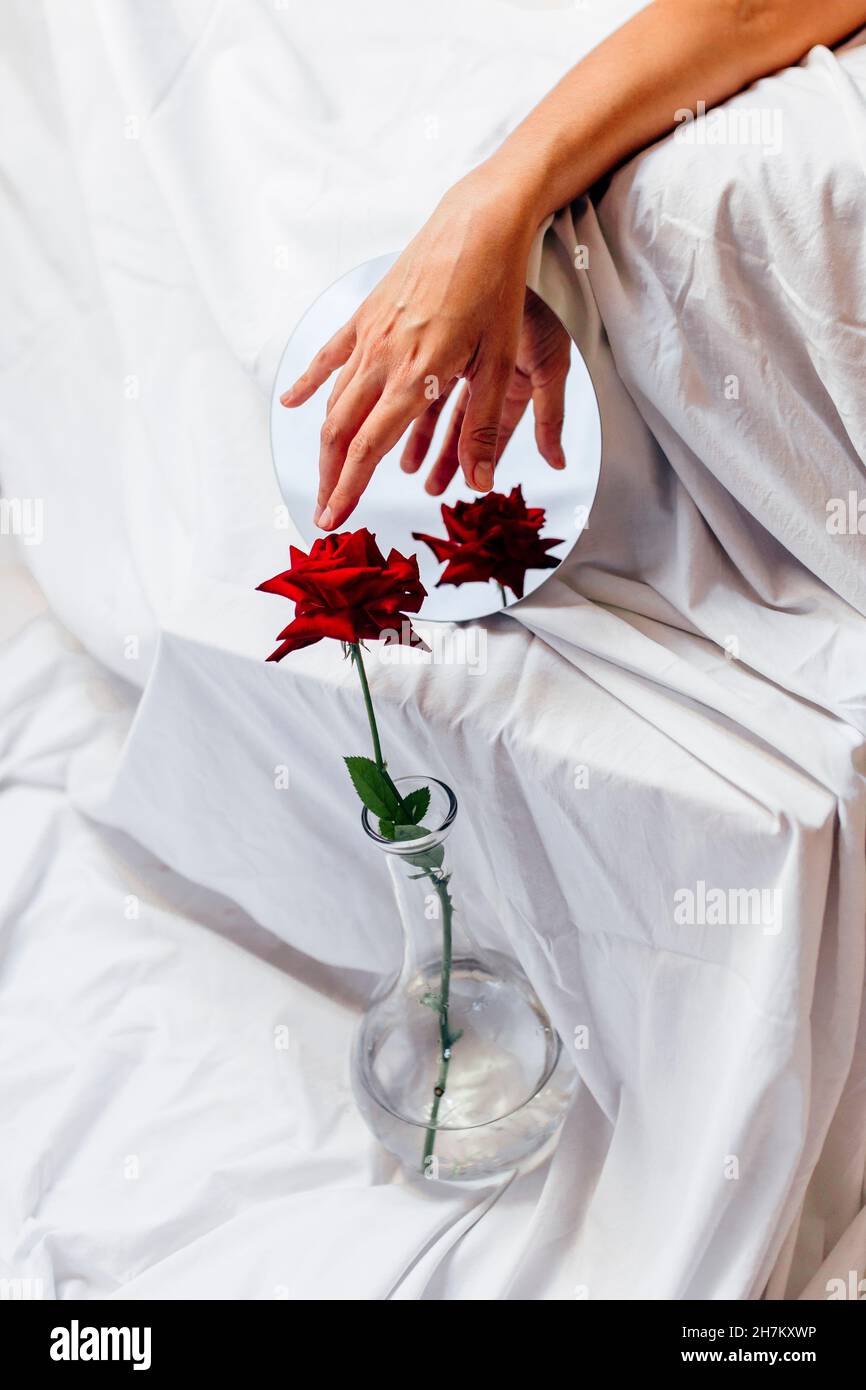 Femme touchant rose rouge dans vase avec réflexion sur miroir Banque D'Images