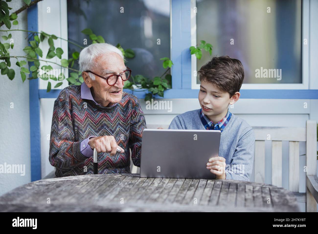 Homme senior parlant avec petit-fils assis avec un PC tablette à la table Banque D'Images